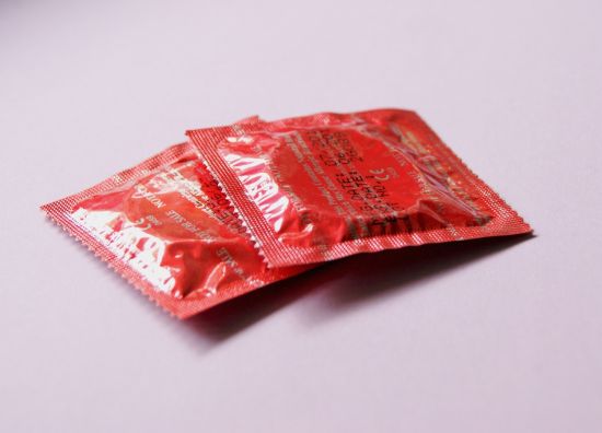 Two red condom wrappers on a light purple background.