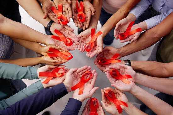 A circle of hands, all skin colors, holding red ribbons symbolizing HIV/AIDS. GettyImages